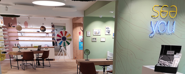 Modernes Optikergeschäft mit Brillenausstellung, Beratungstischen und bunter Deko.